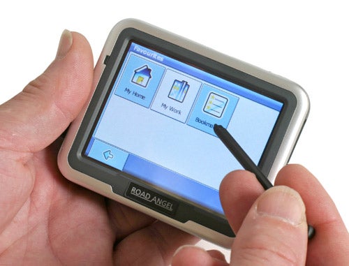 A hand holding the Road Angel Navigator 6000 GPS device with the screen displaying the main menu options including 'My Home', 'My Work', and 'Bookmarks'.