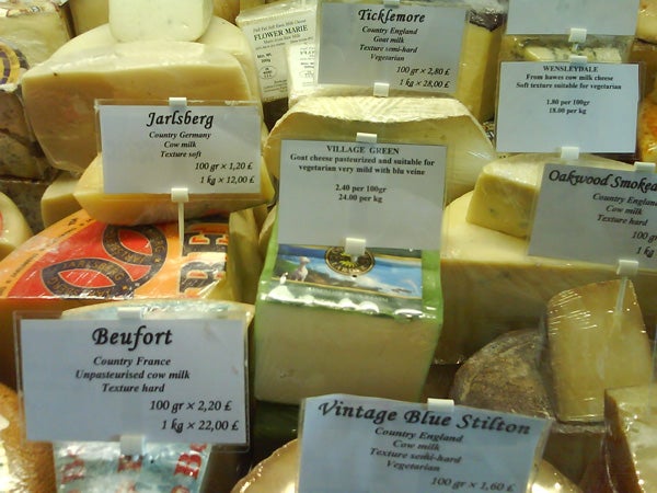 Display of various types of cheese with labels stating the name, country of origin, and price per weight at a cheese counter.