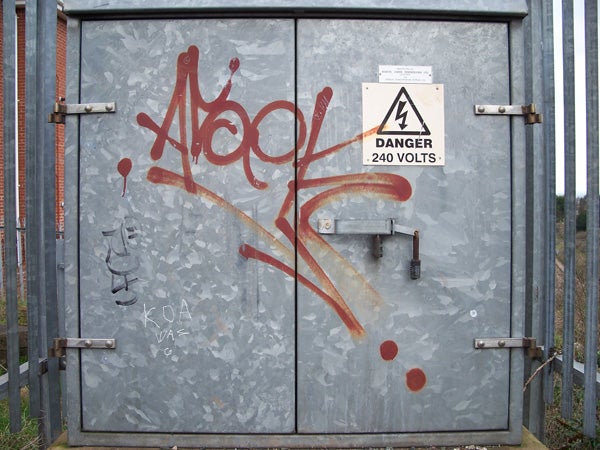 Graffiti on metal electrical box with a warning sign for high voltage.