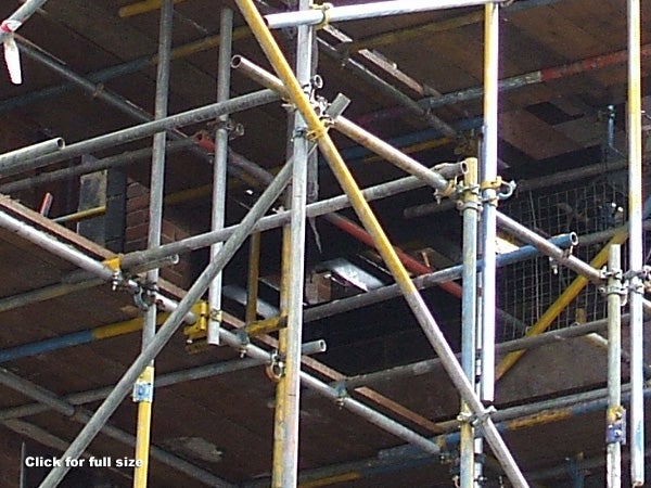 Close-up photo of a construction site showing detailed scaffolding with metal poles and couplers, with a partially visible building in the background, demonstrating the zoom capability of the Fujifilm FinePix A700 camera.