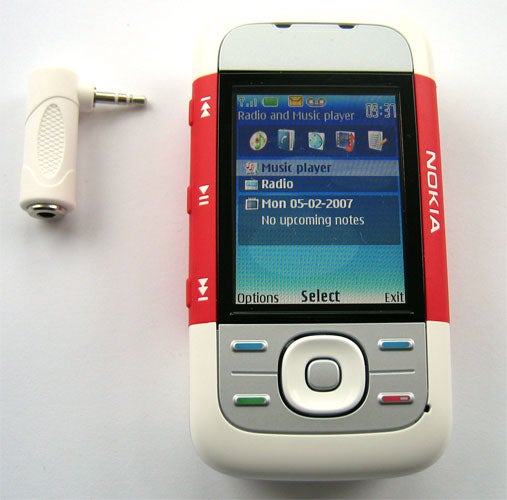 Nokia 5300 XpressMusic mobile phone with red and white color scheme, showing its screen displaying date, music player and radio options, alongside its white earphone accessory.