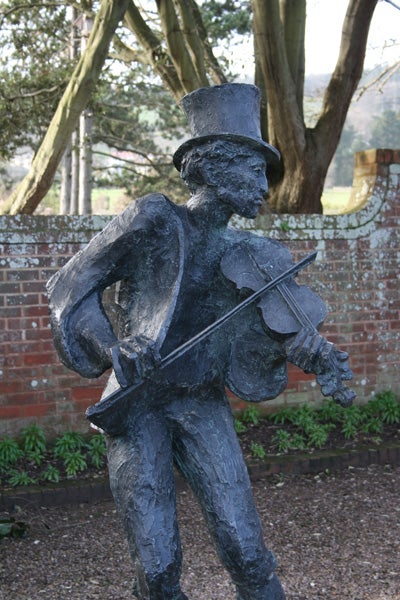 A statue of a man in a top hat playing the violin outdoors.