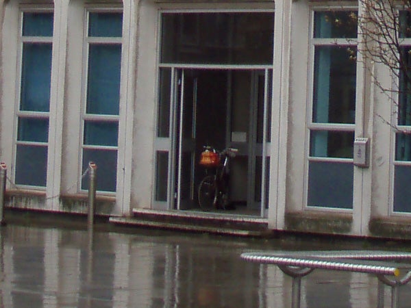 Image of a wet urban scene showing a bicycle parked inside a building's entrance, captured on a rainy day demonstrating the waterproof capability of the Olympus mju 770 SW camera.