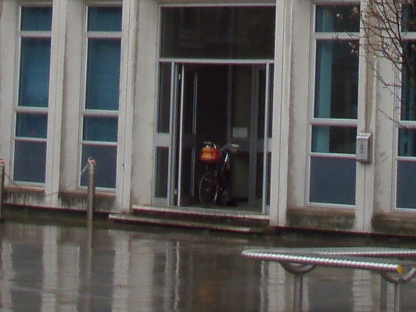 Image taken with Olympus mju 770 SW showing a wet urban scene with a bike parked in the entrance of a building during rain, reflecting the camera's waterproof capabilities.