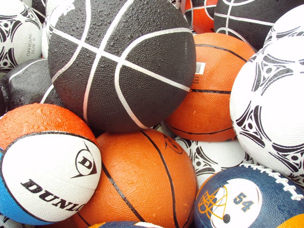 A variety of sports balls clustered together, including basketballs, soccer balls, and an American football, showing a display of textures and colors.
