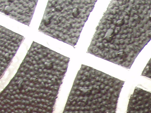 Close-up texture of a black surface with a white grid pattern, possibly a detail of the Olympus mju 770 SW camera exterior or a test surface related to a product review.