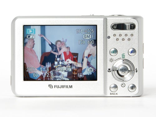 Fujifilm FinePix F20 digital camera displaying a photo on its LCD screen, showing a group of people in a casual indoor setting.