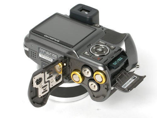 Olympus SP-550UZ digital camera with the battery compartment open showing batteries and memory card slot.