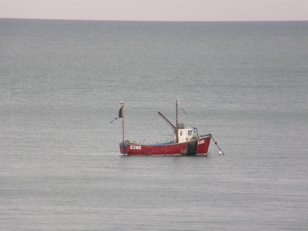 A red and white fishing boat at a standstill on a calm grey sea captured with an Olympus SP-550UZ camera.
