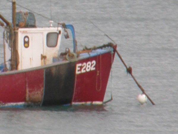 Red and white fishing boat with registration E82 on the hull, moored at sea, demonstrating the zoom capability of the Olympus SP-550UZ camera.
