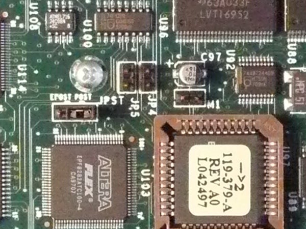Close-up view of electronic circuit board with integrated circuits, resistors, and capacitors, possibly from inside a camera such as the Panasonic Lumix DMC-TZ2 or a similar electronic device.