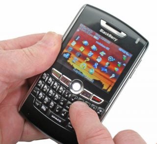 Hand holding a Blackberry 8800 smartphone showing home screen.