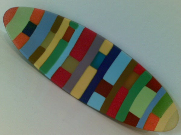 Colorful geometric patterned surfboard-shaped object on a light background.