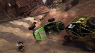 Screenshot from Motorstorm video game showing a dramatic crash with a green off-road vehicle flipping over while another vehicle passes by in a desert racing scene.