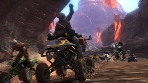 Screenshot from the Motorstorm video game showing ATVs and a motorbike racing on a rugged canyon track with a competitor performing a jump stunt in the foreground.