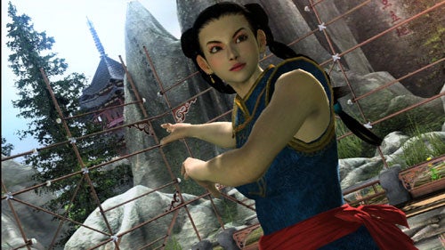A screenshot from the video game Virtua Fighter 5 showing a female character in a blue and gold traditional martial arts outfit with a red sash, posing in a fighting stance with a serene outdoor temple backdrop.