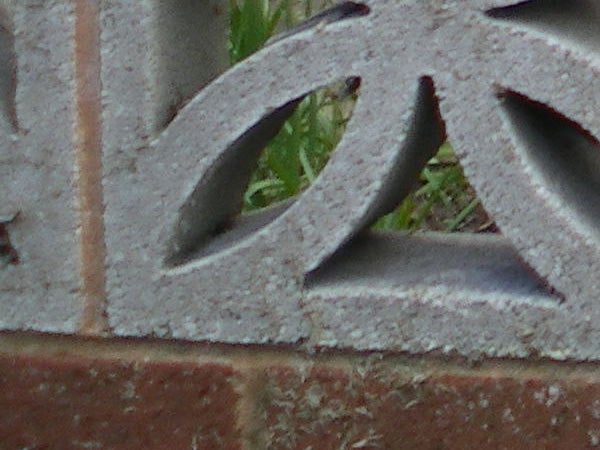 Close-up of a decorative brick wall with a frosty texture, showing a section of a cast iron decorative grill with geometric patterns.