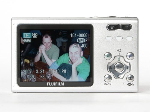 Fujifilm FinePix Z5fd digital camera displaying a photo of two people on its LCD screen, showing camera settings and date on the display, with silver body and control buttons on the right.
