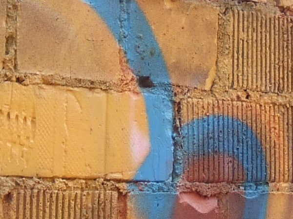 Close-up photo of a textured brick wall with blue and orange graffiti, showcasing the color capture and detailing capability of the Fujifilm FinePix Z5fd camera.