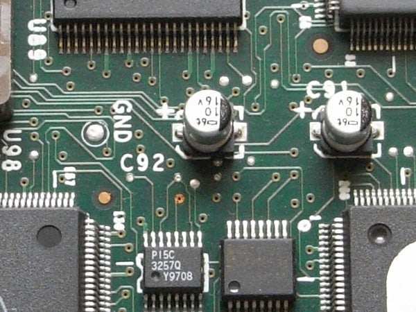 Close-up of electronic circuit board with capacitors, resistors, and integrated circuits, potentially from inside a device such as the Ricoh Caplio R6 digital camera.