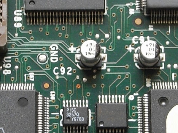 Close-up view of an electronic circuit board with various components including capacitors, chips, and connectors, possibly from inside a Ricoh Caplio R6 camera.