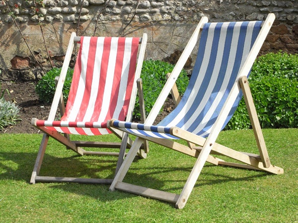 Two deck chairs with red and white stripes and blue and white stripes respectively, on a sunny day with green grass and a stone wall in the background, possibly taken with a Ricoh Caplio R6 camera.