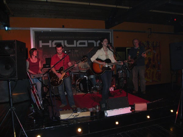 A band performing on stage in a dimly lit venue with the audience not visible in the shot.