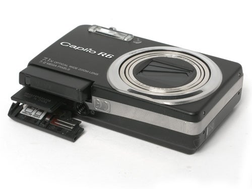 Black Ricoh Caplio R6 digital camera with the battery compartment open, showing the battery and SD card slot.