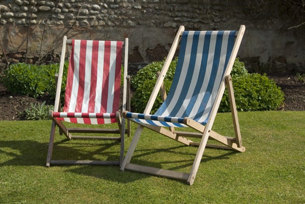 Two deck chairs with red and white stripes and blue and white stripes on a green lawn with a stone wall in the background.