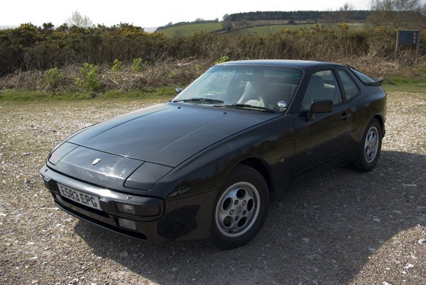 Black vintage sports car parked on gravel with grassy field in the background.