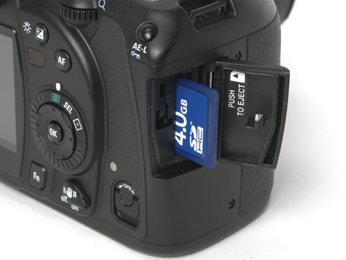Close-up of a black Samsung GX-10 DSLR camera with an open SD card slot, showcasing a blue 4GB SD card partially inserted.