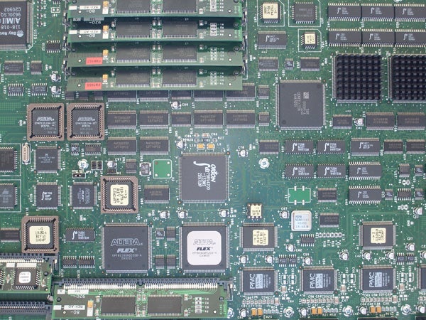 Close-up view of a green printed circuit board with various integrated circuits, memory modules, and electronic components.
