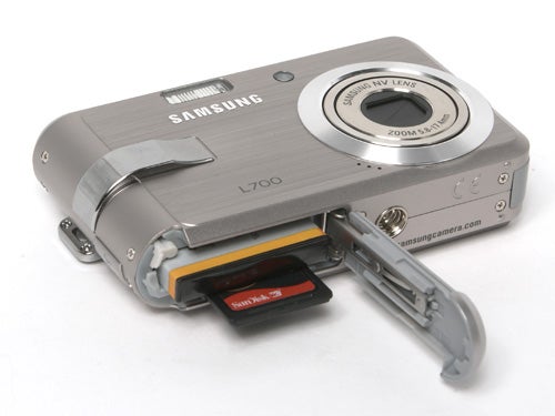 Samsung L700 digital camera with the battery compartment open showing a battery and memory card inserted.