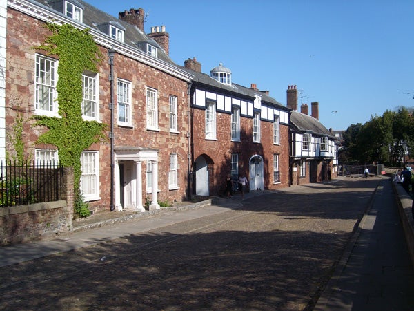 The image depicts a cobblestone-lined street flanked by historical buildings, one covered in creeping ivy, under a clear blue sky. This scene does not show a Samsung L700 or any related product context and appears to be a streetscape rather than an image from a product review.