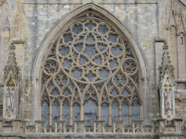Detailed Gothic architecture of a cathedral rose window with intricate stone tracery and statues.