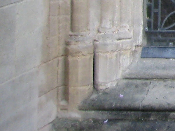Photograph taken with a Canon Digital IXUS 70 camera showing the close-up of an old sandstone building's corner, demonstrating the camera's resolution and color reproduction. The image is slightly blurry, indicating either movement during capture or a focus issue.