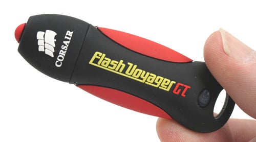 A person holding a Corsair Flash Voyager GT 8GB USB flash drive with a black and red rubber casing and the logo and product name printed on the side.