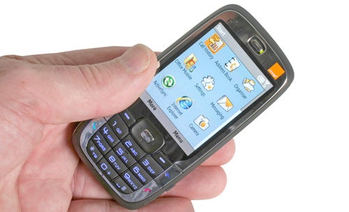 Hand holding an Orange SPV E650 smartphone with a visible QWERTY keyboard and the screen displaying the Windows Mobile operating system interface.