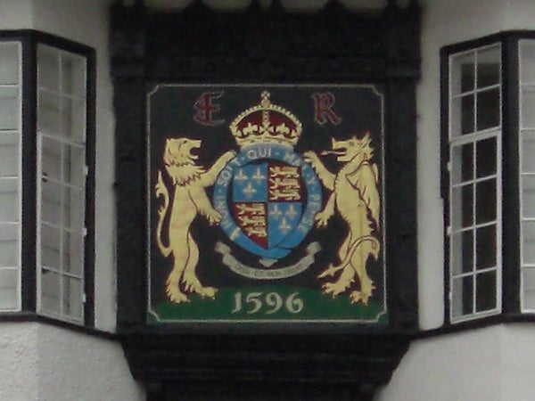 The image shows a coat of arms with a crowned shield flanked by two lions, featuring an inscription of 