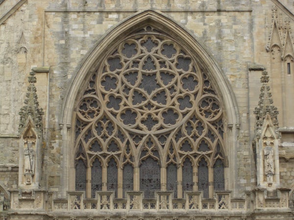 The image shows an intricate gothic-styled stone window on a cathedral wall, featuring detailed tracery and statues mounted on the sides, but it is not related to Casio Exilim EX-Z1050 or any product review.