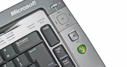 Close-up view of the Microsoft Wireless Entertainment Desktop 7000 keyboard, focusing on the upper right section with multimedia keys and the Windows logo on a silver and black background.