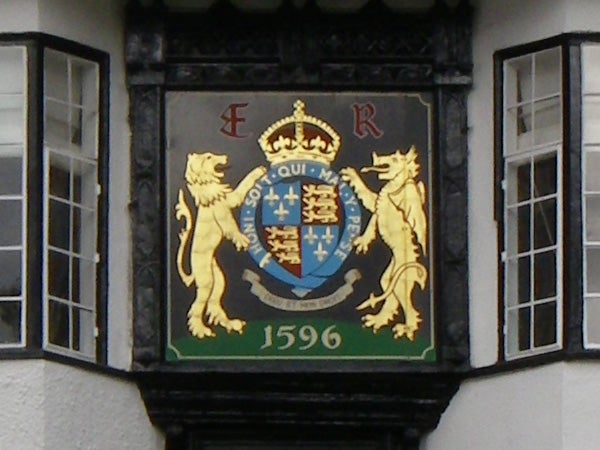 A close-up photo of a royal crest with a shield, two lions, and a crown, mounted on a building façade.