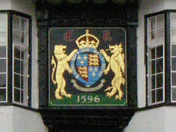 Colorful coat of arms on a building facade featuring a crowned shield flanked by two lions with the inscription 