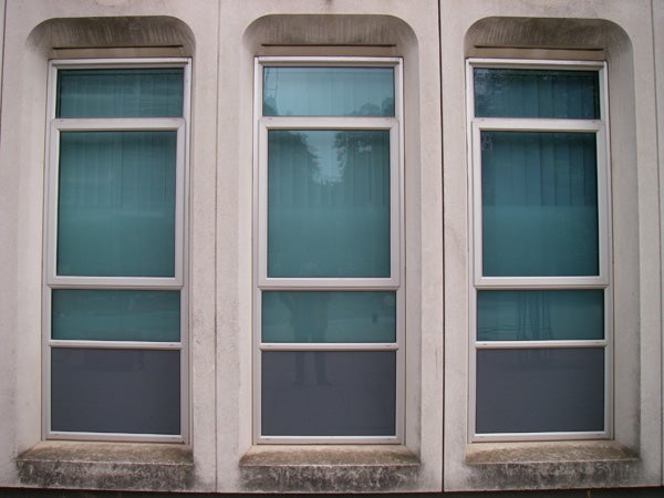 Three tall vertical windows on a concrete building wall with reflections visible on the glass surfaces.