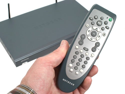 Hand holding the Netgear Digital Entertainer HD EVA8000 remote control with the main unit in the background.