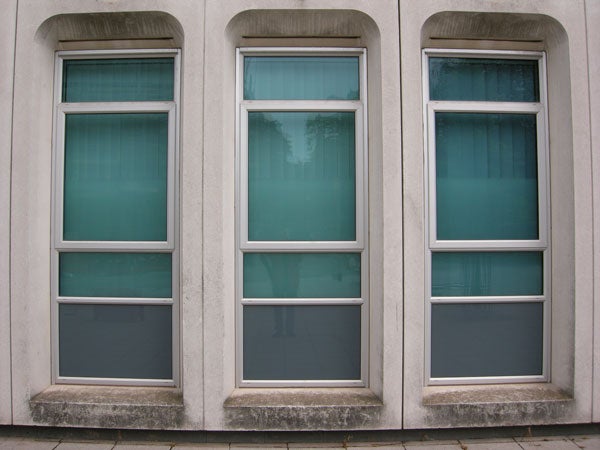 Three teal windows on a grey concrete wall.