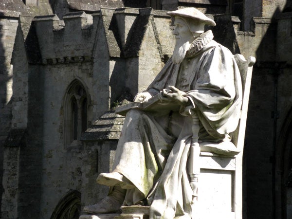 Statue of a historical figure seated with a building background.