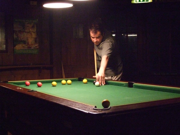 Person playing pool in dimly lit room, low-light photography test.