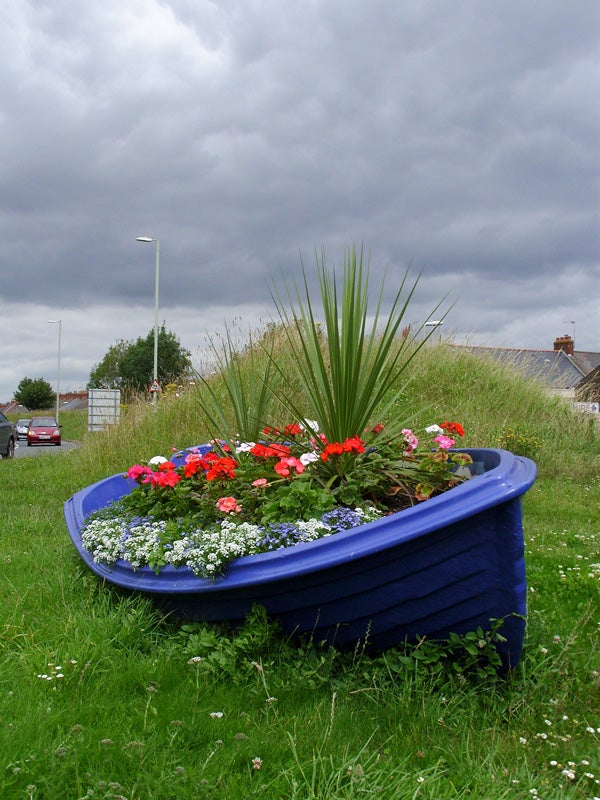 Colorful flowers in a blue boat-shaped planter under cloudy skies.