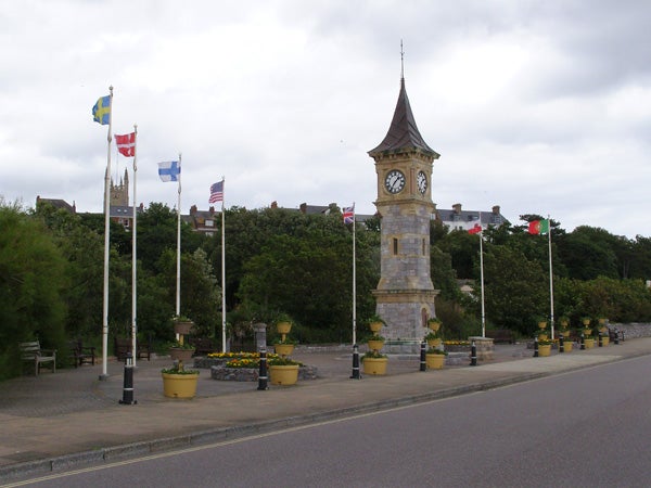 Stone clock tower with international flags along a street.